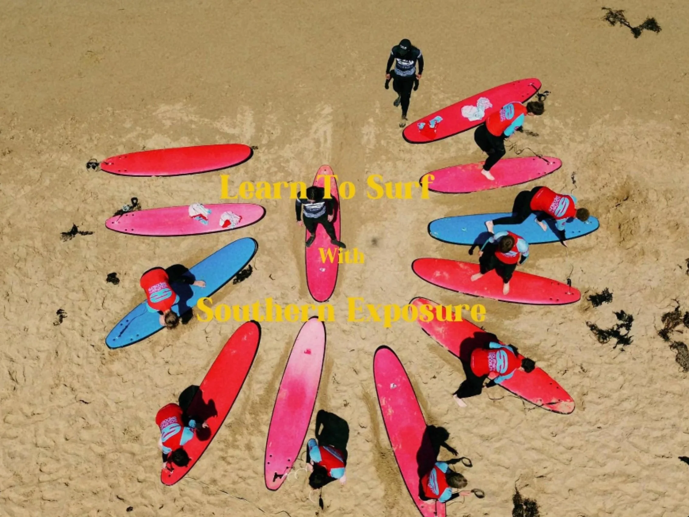 Eight people on surfboards arranged in a circle on a sandy beach, with some people standing and others preparing to surf. Text overlay reads 'Learn To Surf With Southern Exposure'.