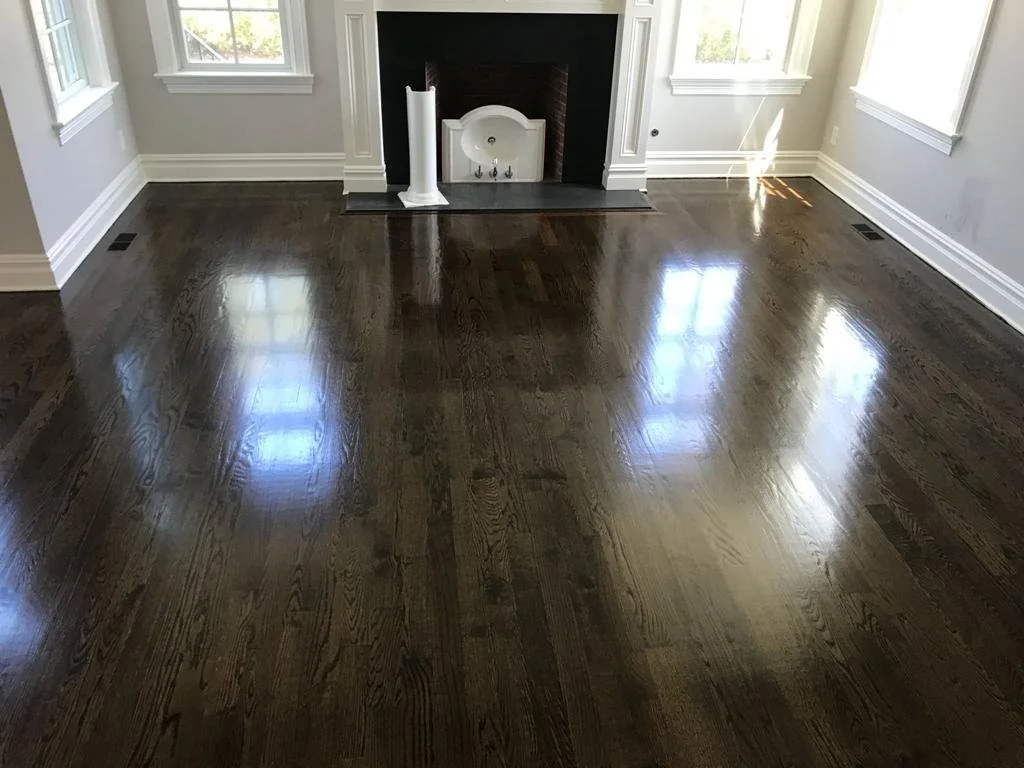 Empty living room with dark wood floors, white walls, a fireplace, and windows allowing natural light.
