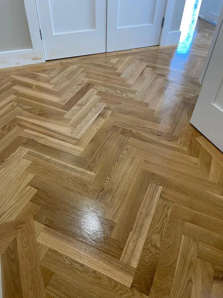 Close-up of a wooden parquet floor with a herringbone pattern near white double doors.
