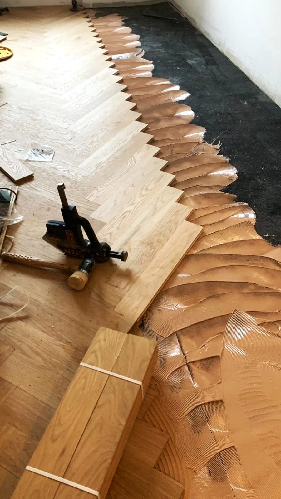 Wood flooring installation with overlapping copper-colored underlayment and new oak hardwood planks, along with tools.