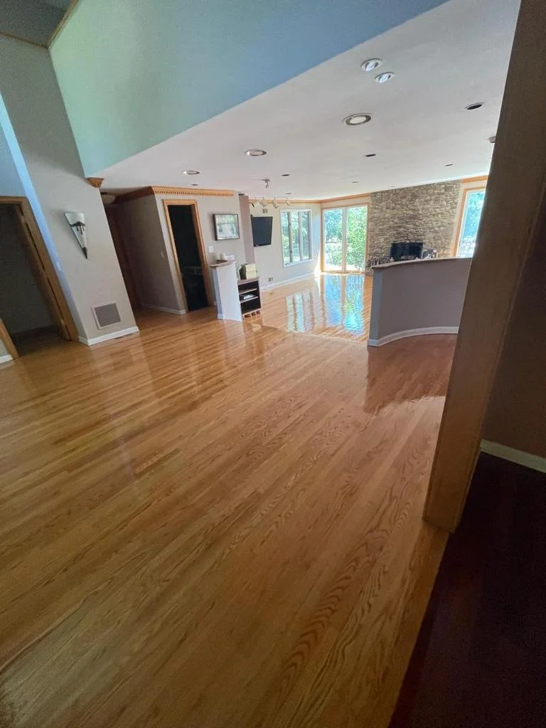 Empty living room with hardwood floors, large windows, fireplace, and TV mounted on wall.
