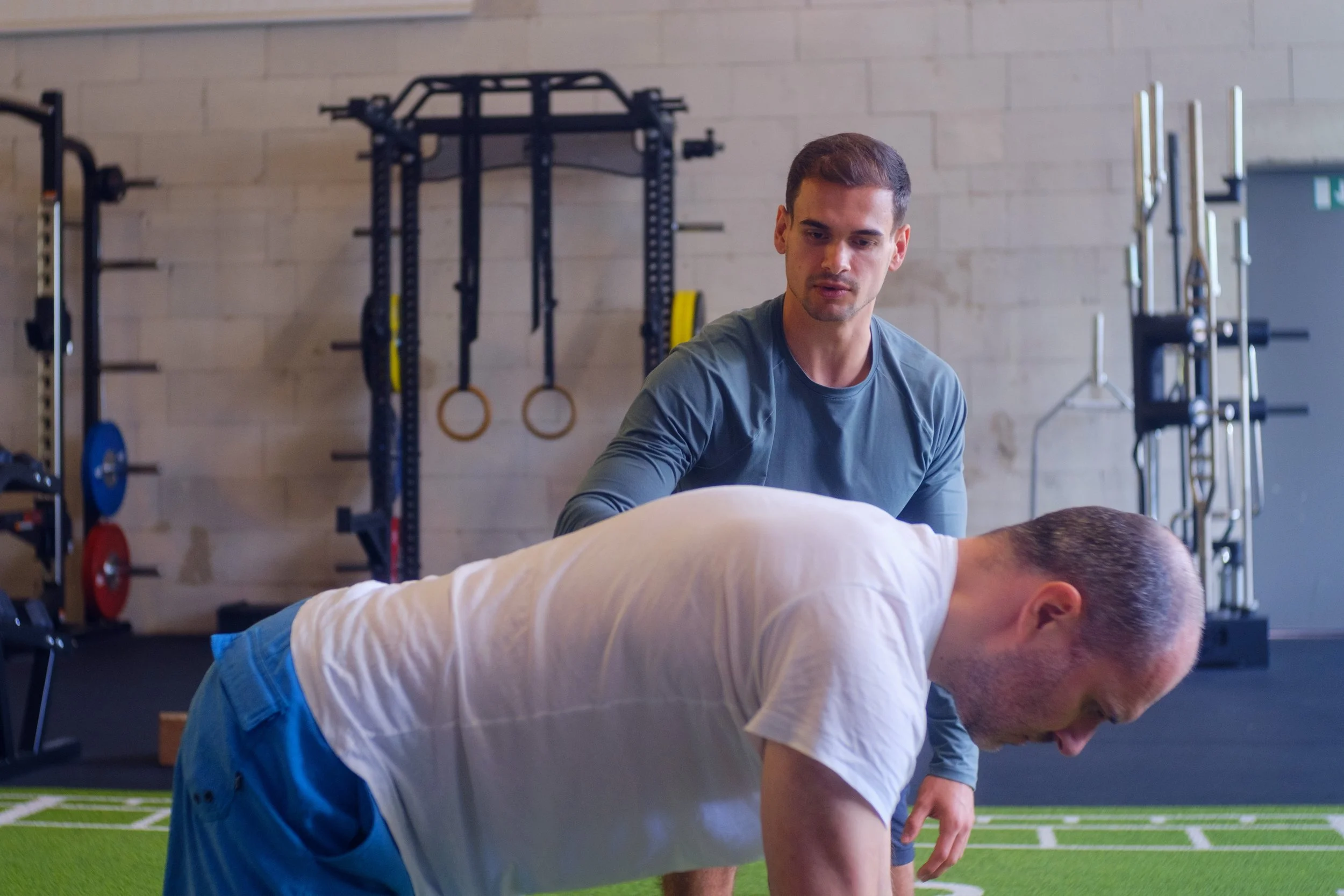 Personal Trainer hilft einem Mann bei einer Übung im Fitnessstudio.
