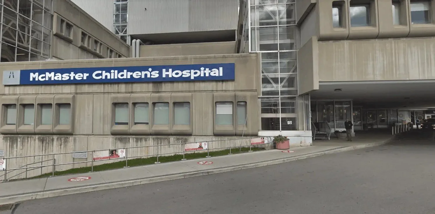 Exterior of McMaster Children's Hospital building with a large blue and white sign, concrete facade, and glass entrance area.