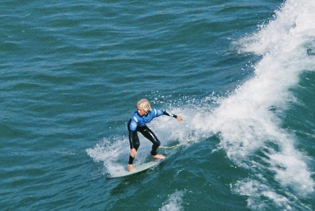 Person surfing on a wave in the ocean, wearing a blue jacket and black wetsuit.