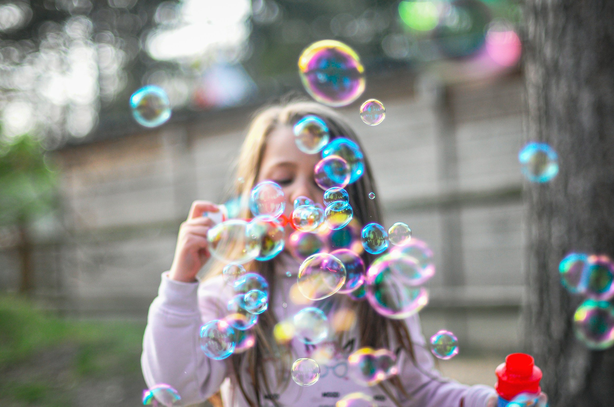 A girl playing with colorful soap bubbles outdoors in a blurred background.