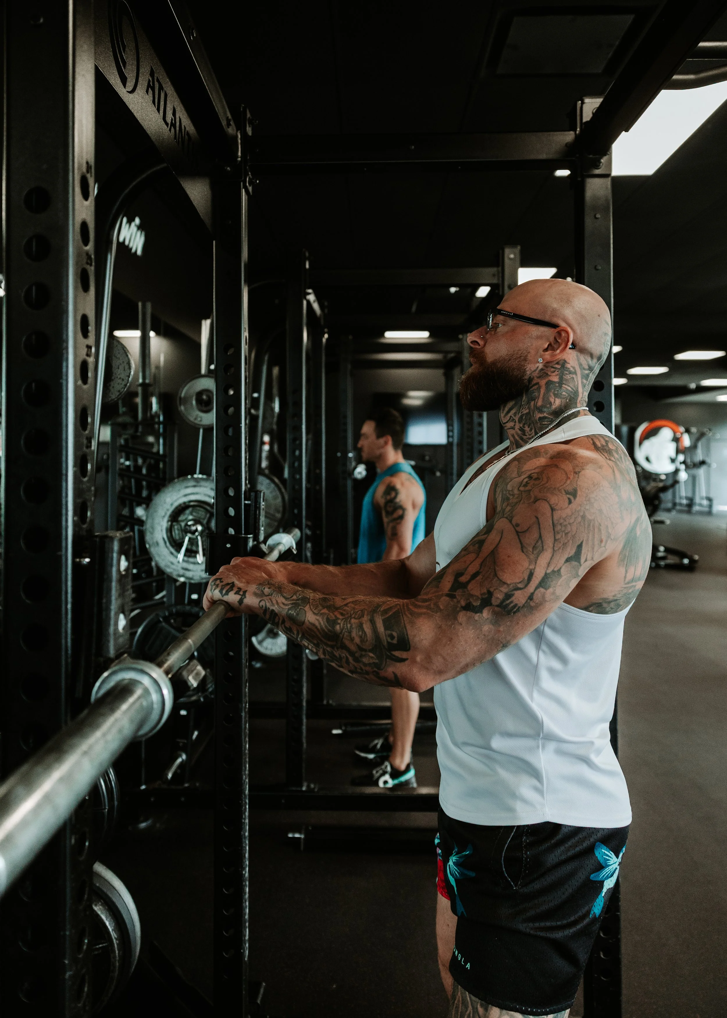 A muscular man in black shorts and sneakers is preparing to lift a barbell in a dark gym.