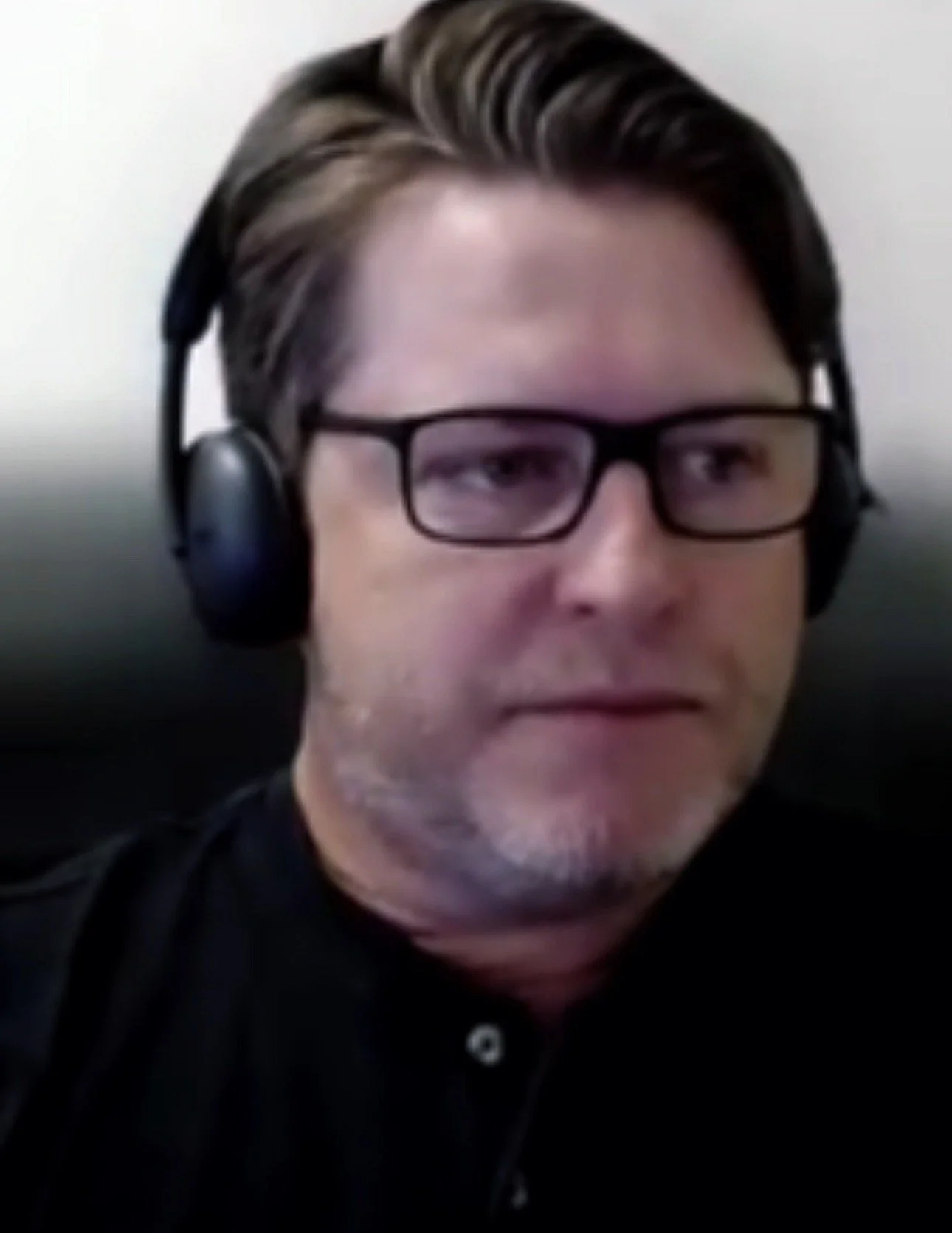 A man with glasses and headphones, looking at the camera