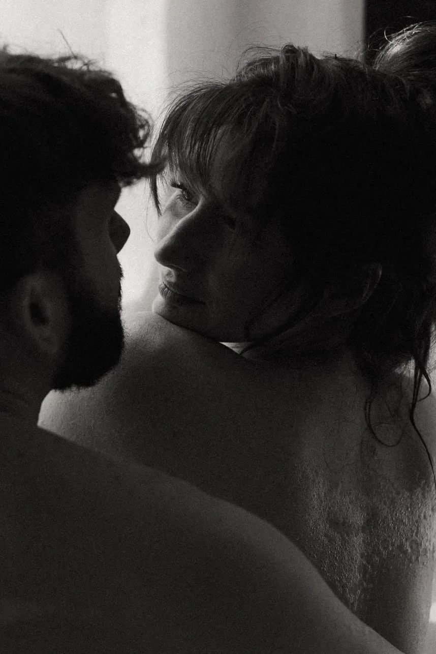 Black and white image of a close-up of a couple, focusing on a woman looking over her shoulder at a man.