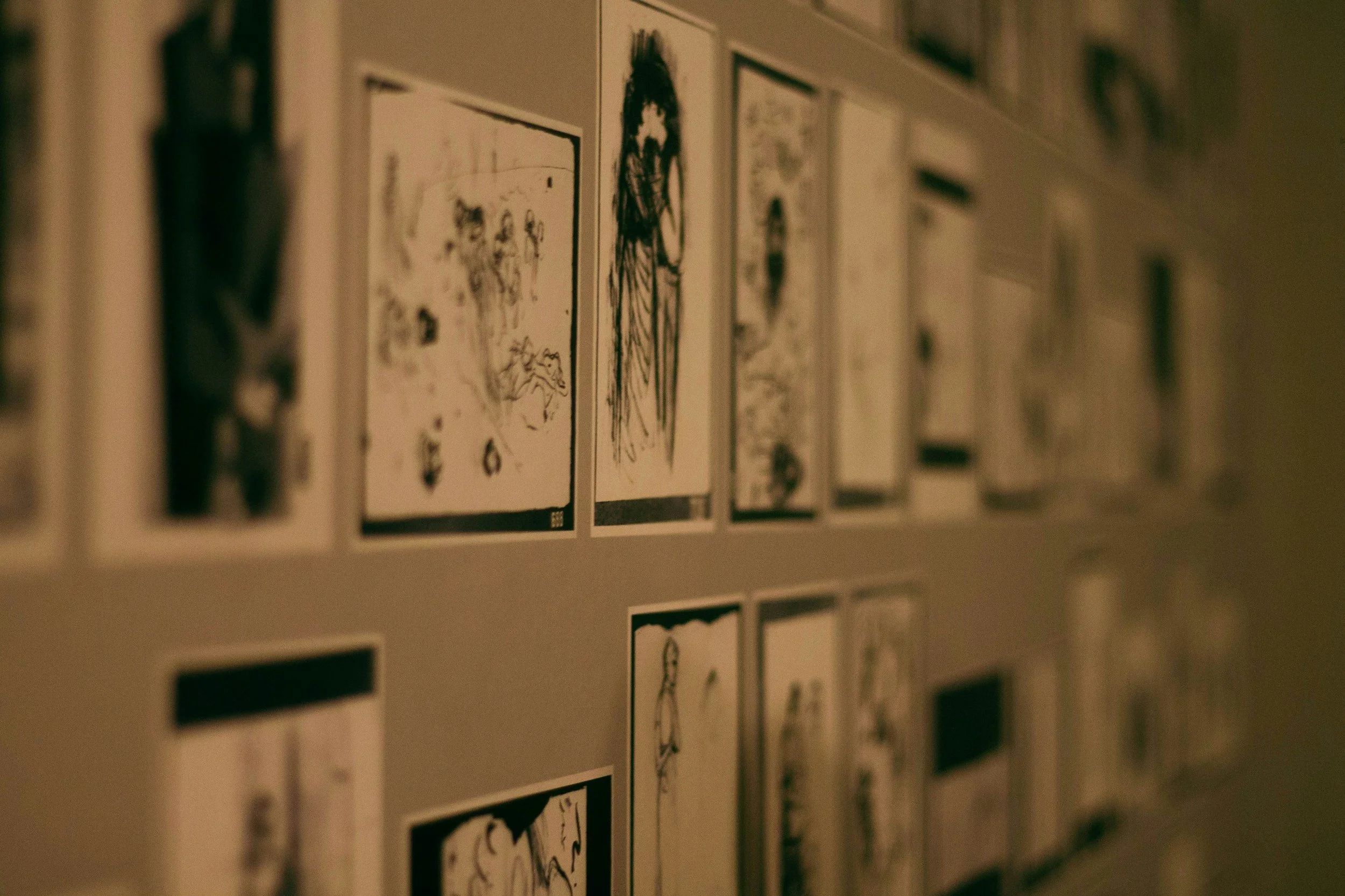Wall with multiple black-and-white sketches or comic strips displayed in frames, arranged in horizontal rows.