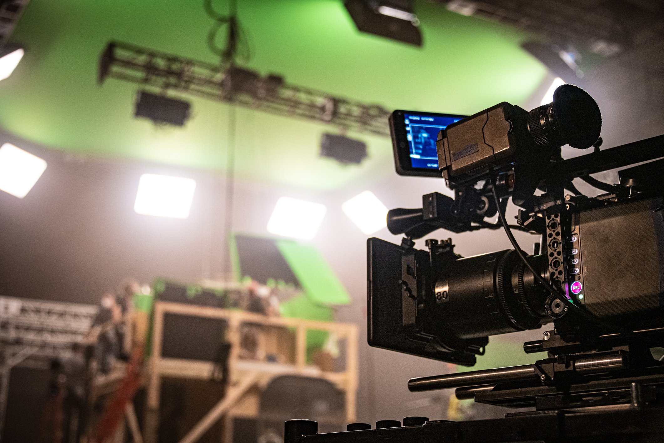 Close-up of a professional camera on a film set, with bright lights and green screen background.