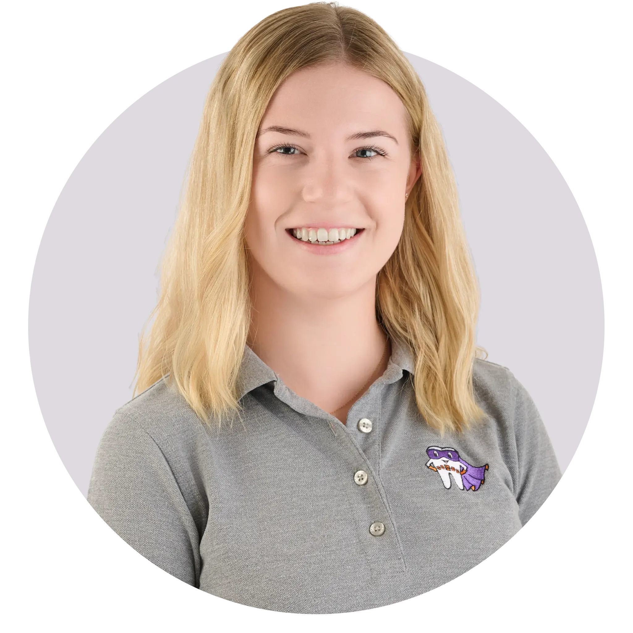 Lächelnde Frau mit blonden Haaren, trägt graues Polo mit Drachenspielzeug auf dem linken Brustbereich.