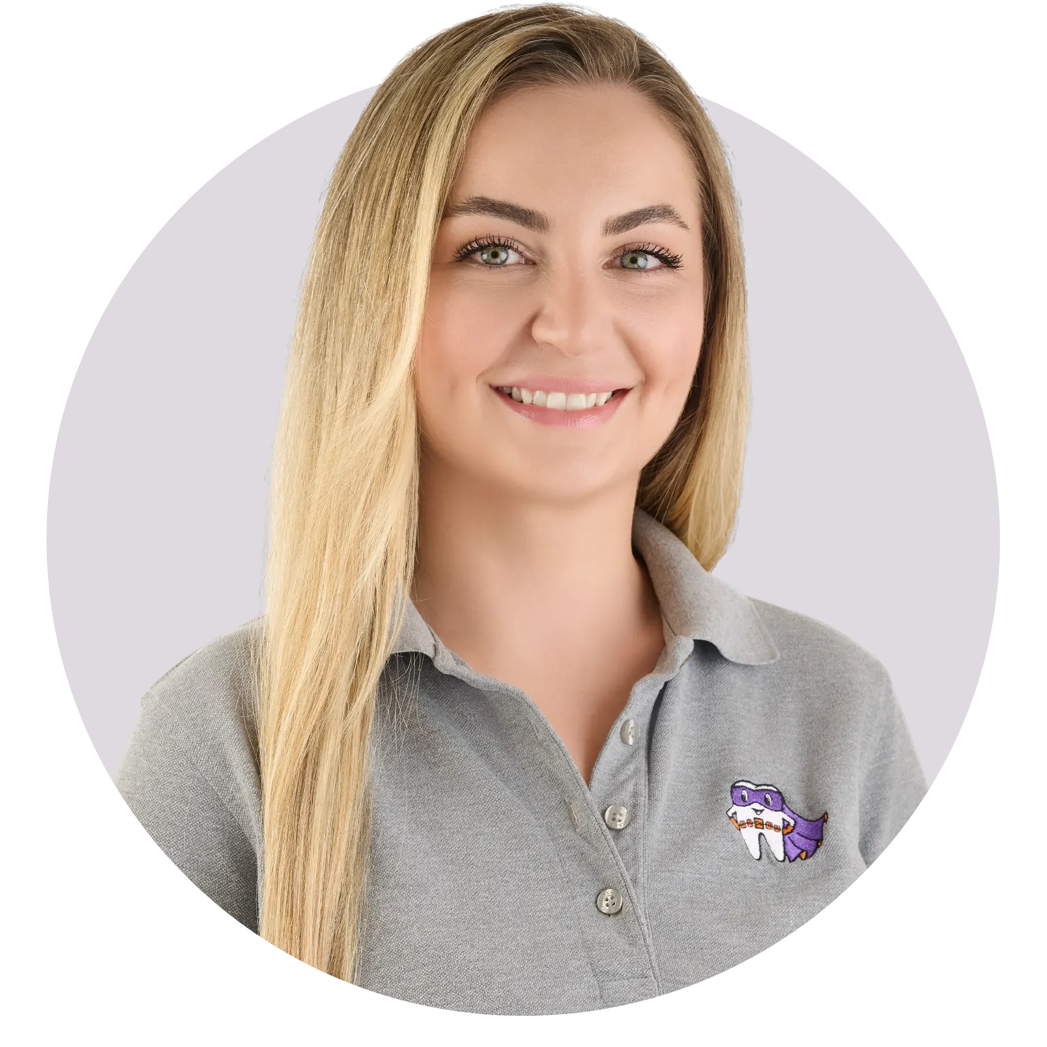 Ein Lächelndes Mädchen mit langem blondem Haar trägt ein graues Polo-Shirt mit einer Zahn-Maskottchen-Pin of einem Zahn mit lustigem Gesicht, auf einem hellen Hintergrund.