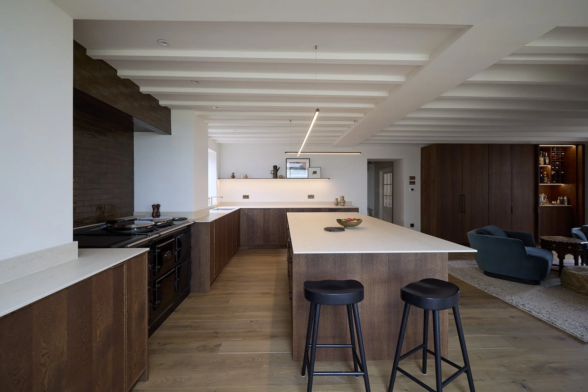 Open-plan kitchen and living space with dark timber joinery and layered lighting at The Old Vicarage in Derbyshire by Boyes Design