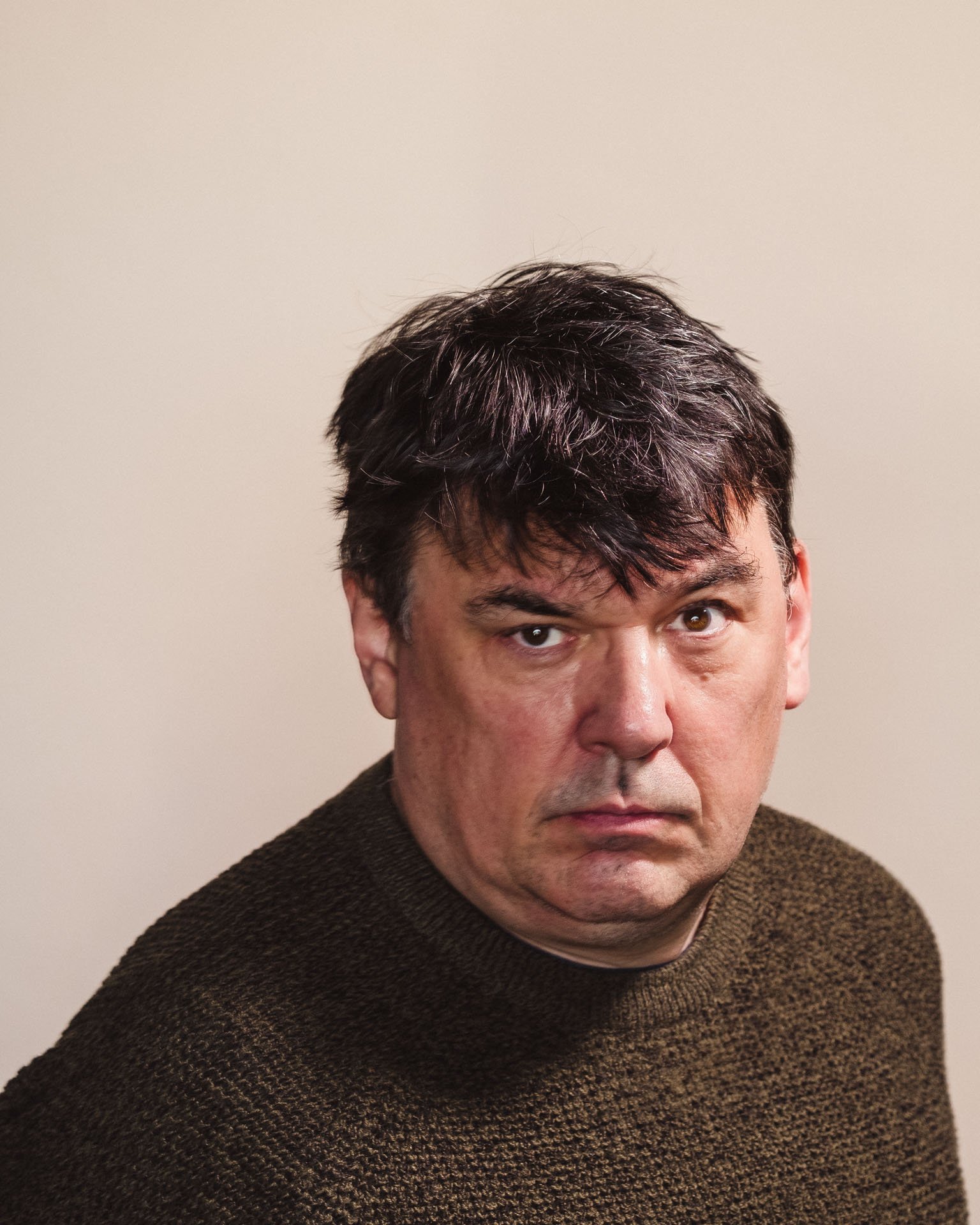 Graham Linehan with dark brown hair wearing a brown textured sweater against a plain beige background.