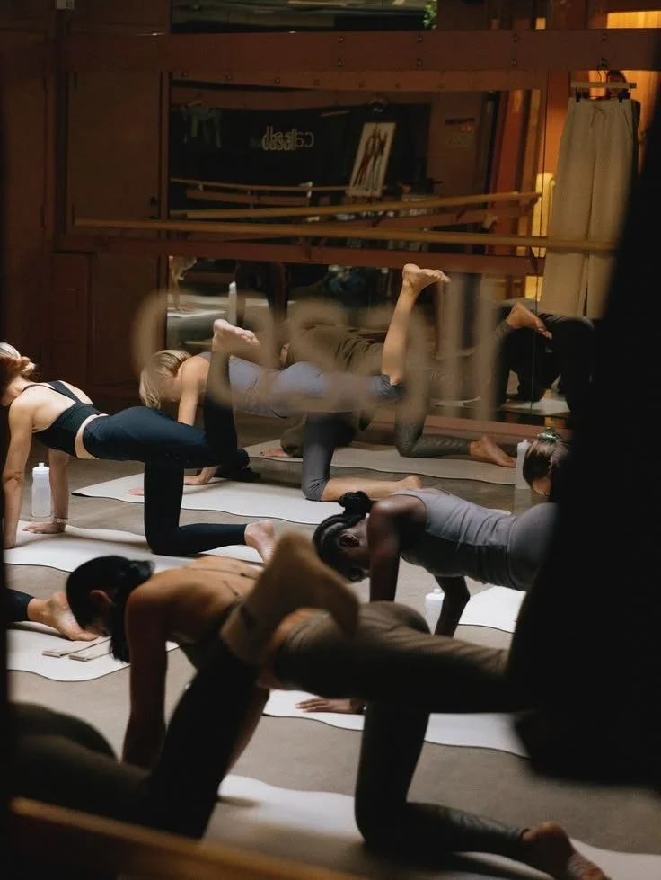 People participating in a yoga class in a studio with wooden walls and mirrors, practicing various poses on yoga mats.
