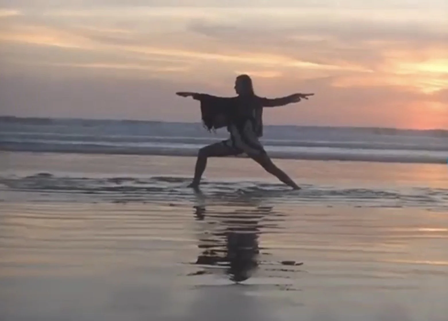 Person performing a yoga pose on the beach at sunset, with waves and sky in the background.