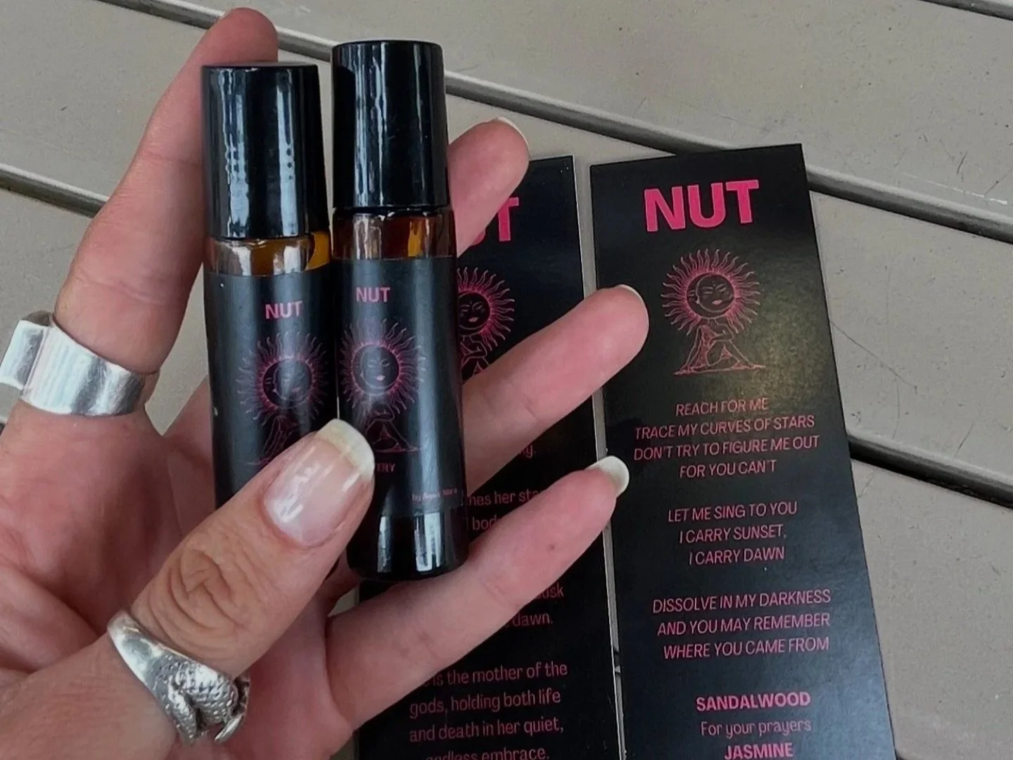 Hand holding two small bottles with black caps labeled 'NUT', set against a background of a black and pink informational flyer.