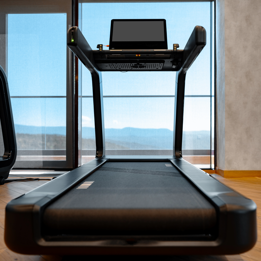 Modern treadmill with a screen, positioned indoors near large windows showing a view of mountains.