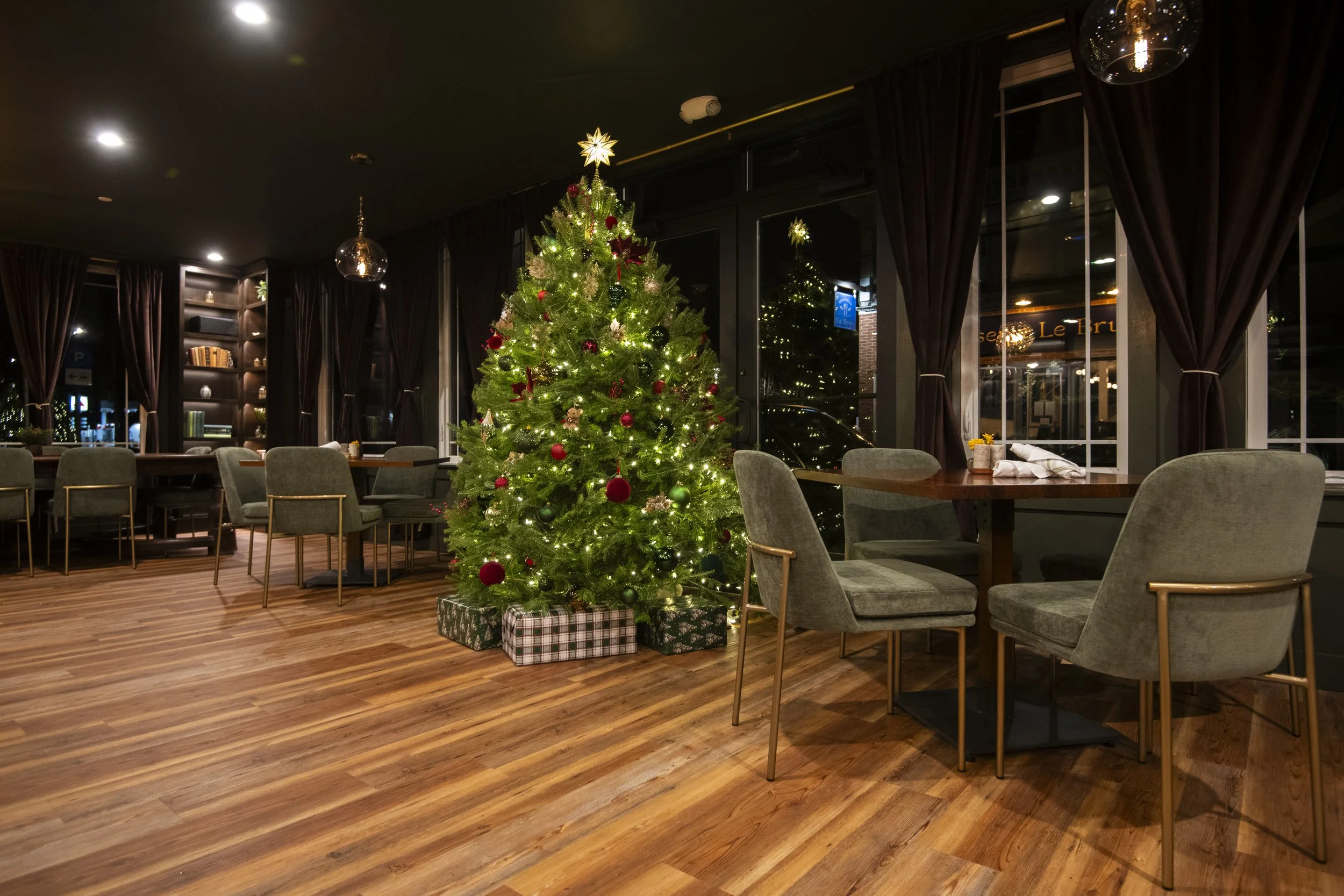 Empty restaurant with wooden floors, decorated Christmas tree with presents, and dark curtains.
