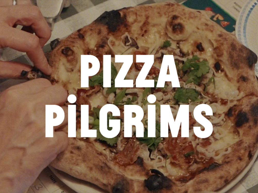 A pizza with various toppings including cilantro, cheese, and meat, with two hands grabbing a slice.