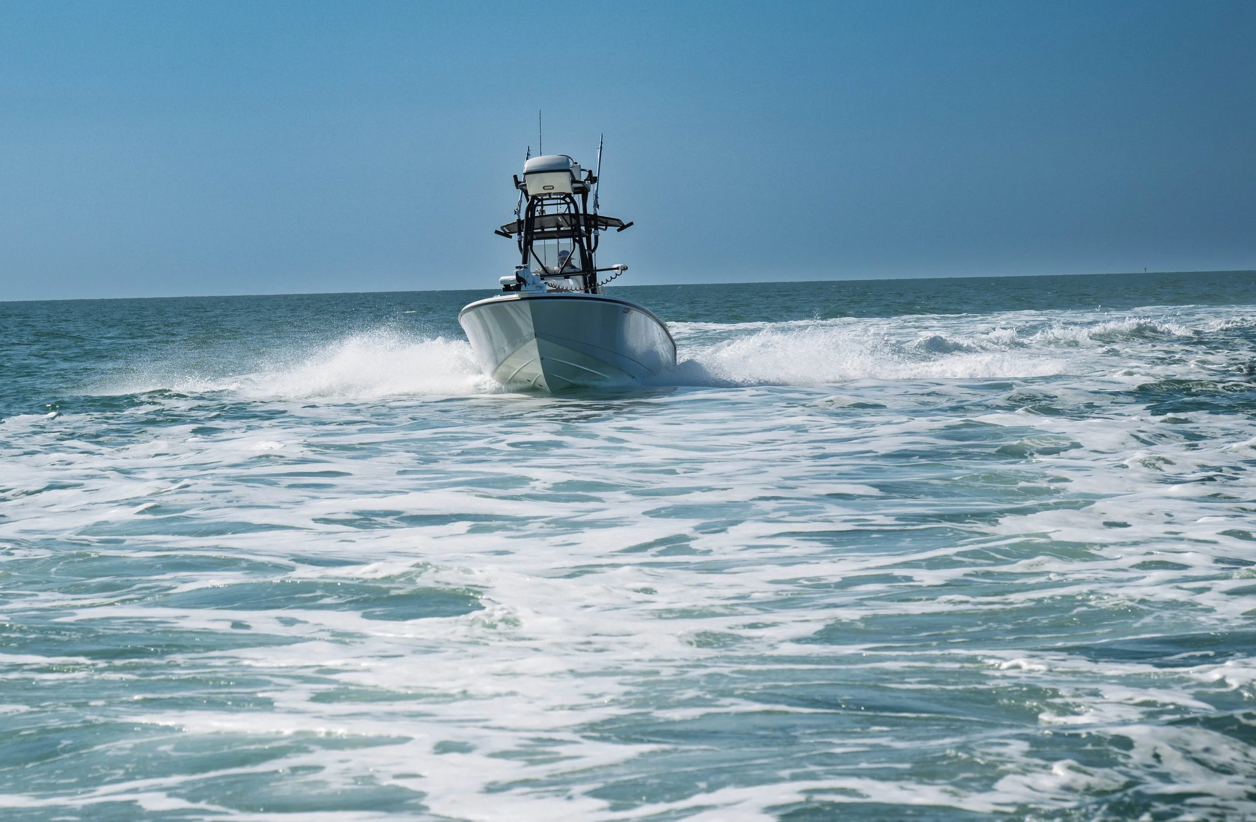A motorboat moving at high speed through the ocean, creating waves and foam behind it under a clear blue sky.