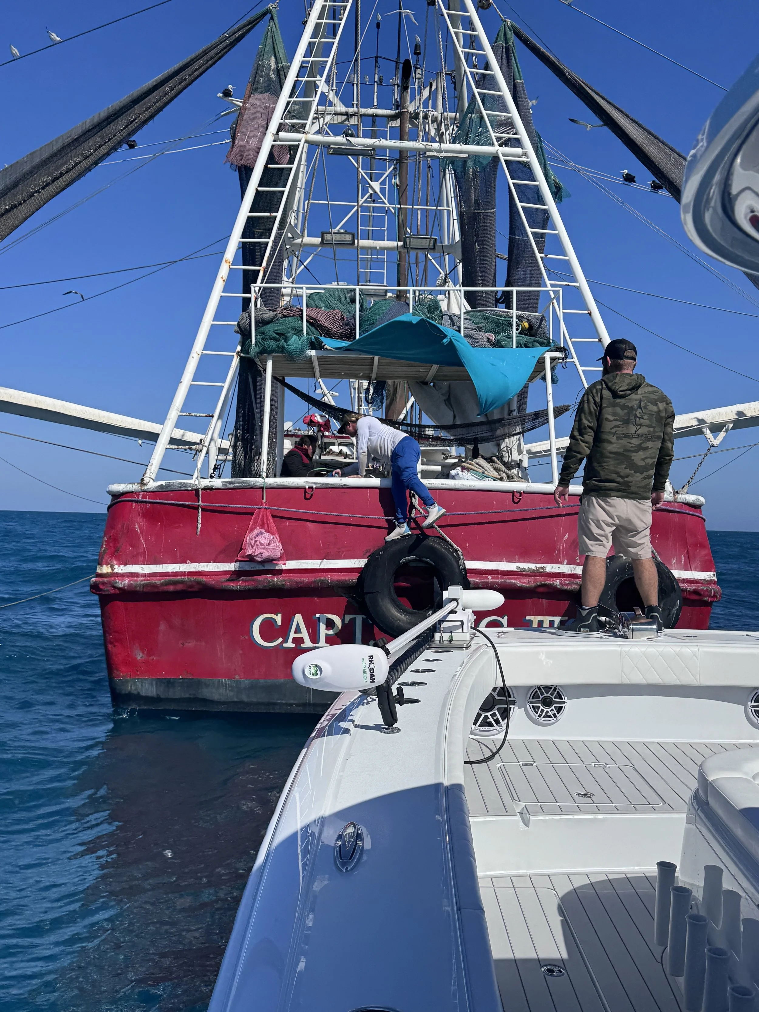People working on a red and white fishing boat named 'Captain' in the ocean on a clear, sunny day.