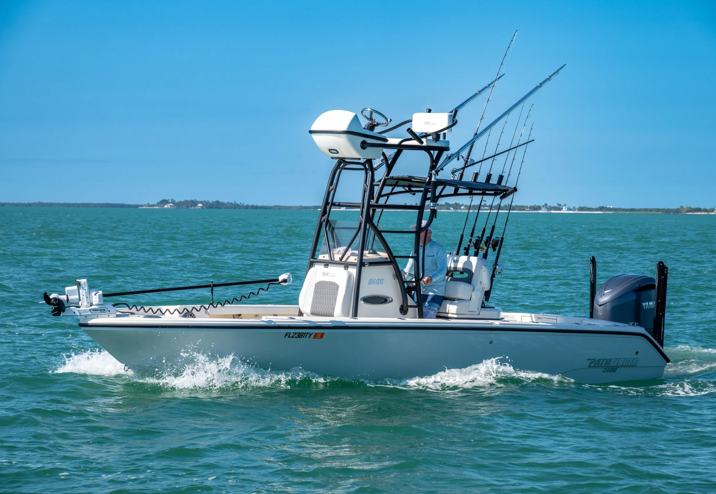 A fishing boat with multiple fishing rods, a person on the boat, and a Yamaha engine, on open water under a blue sky.