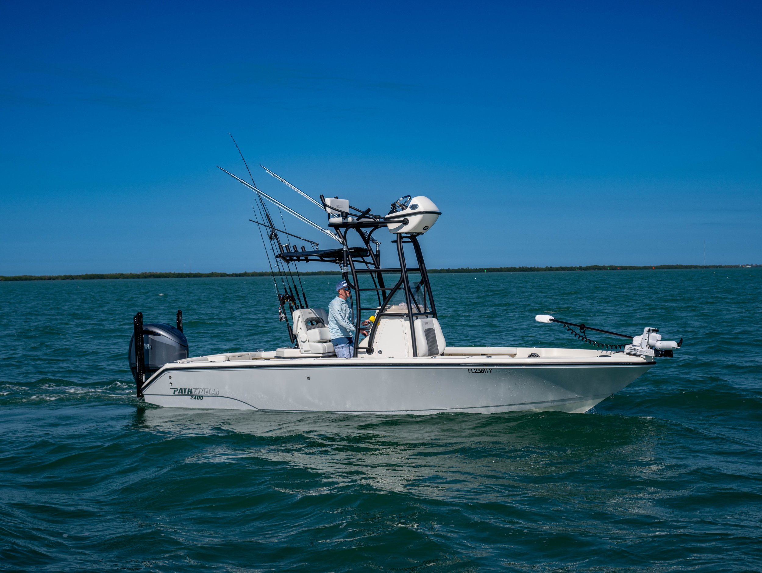 A white fishing boat with fishing rods on board sailing on a blue body of water under a clear sky.