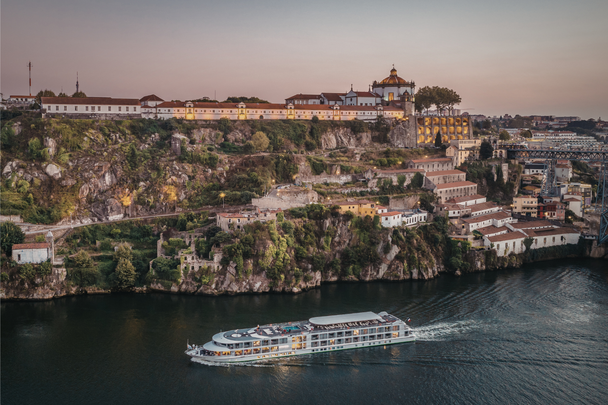 a european river cruise boat sailing next to a historic cliffside town.