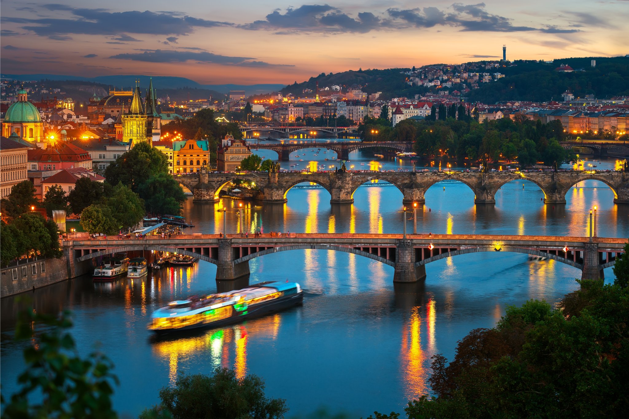 Illuminated bridges in Prague with river cruise ships.