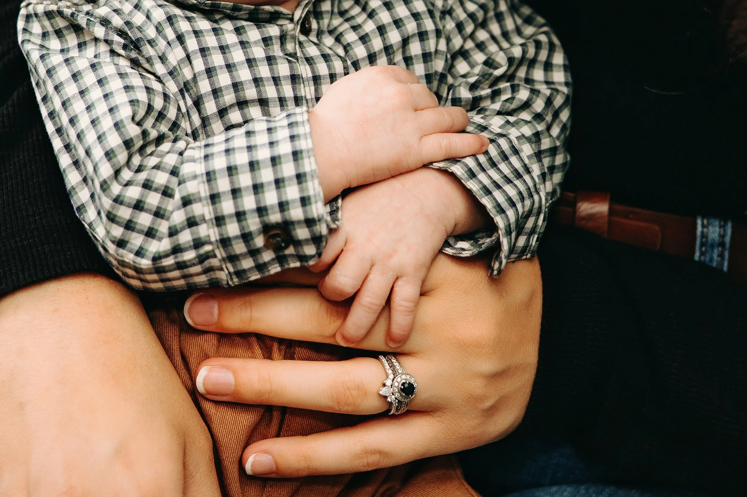 Close-up of a child's hand resting on an adult's lap, with the adult wearing a ring with a dark stone and diamonds.