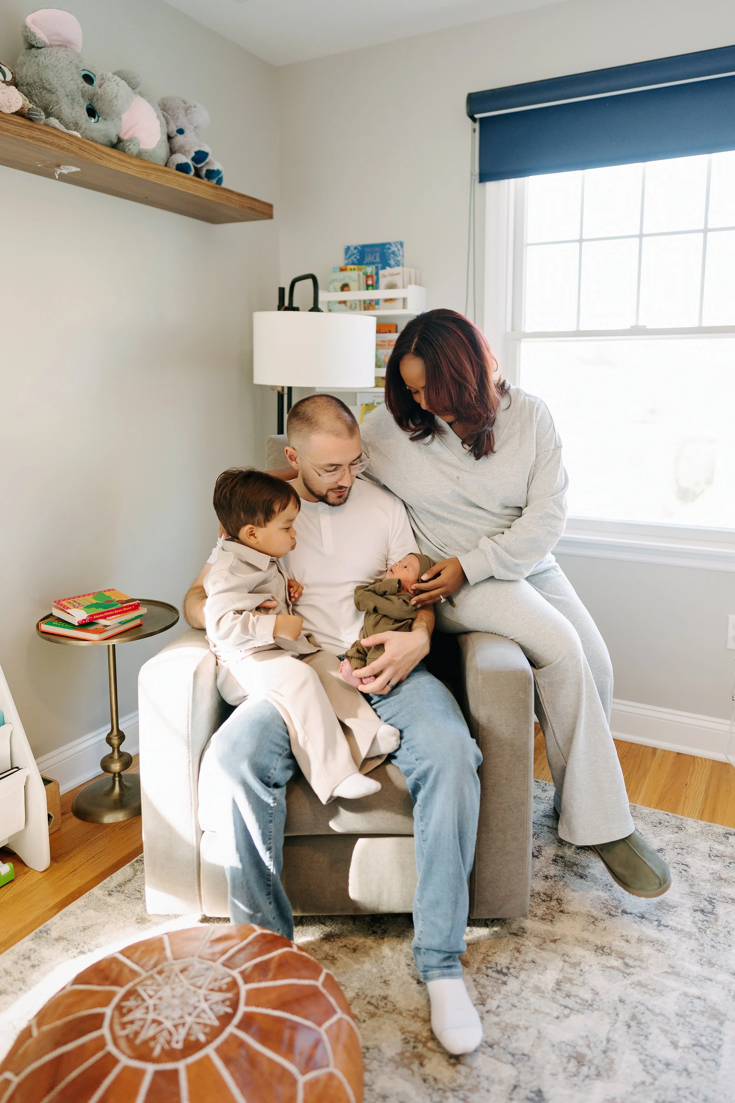 Family sitting together in a cozy living room, holding their newborn baby, with a child sitting on dad's lap.