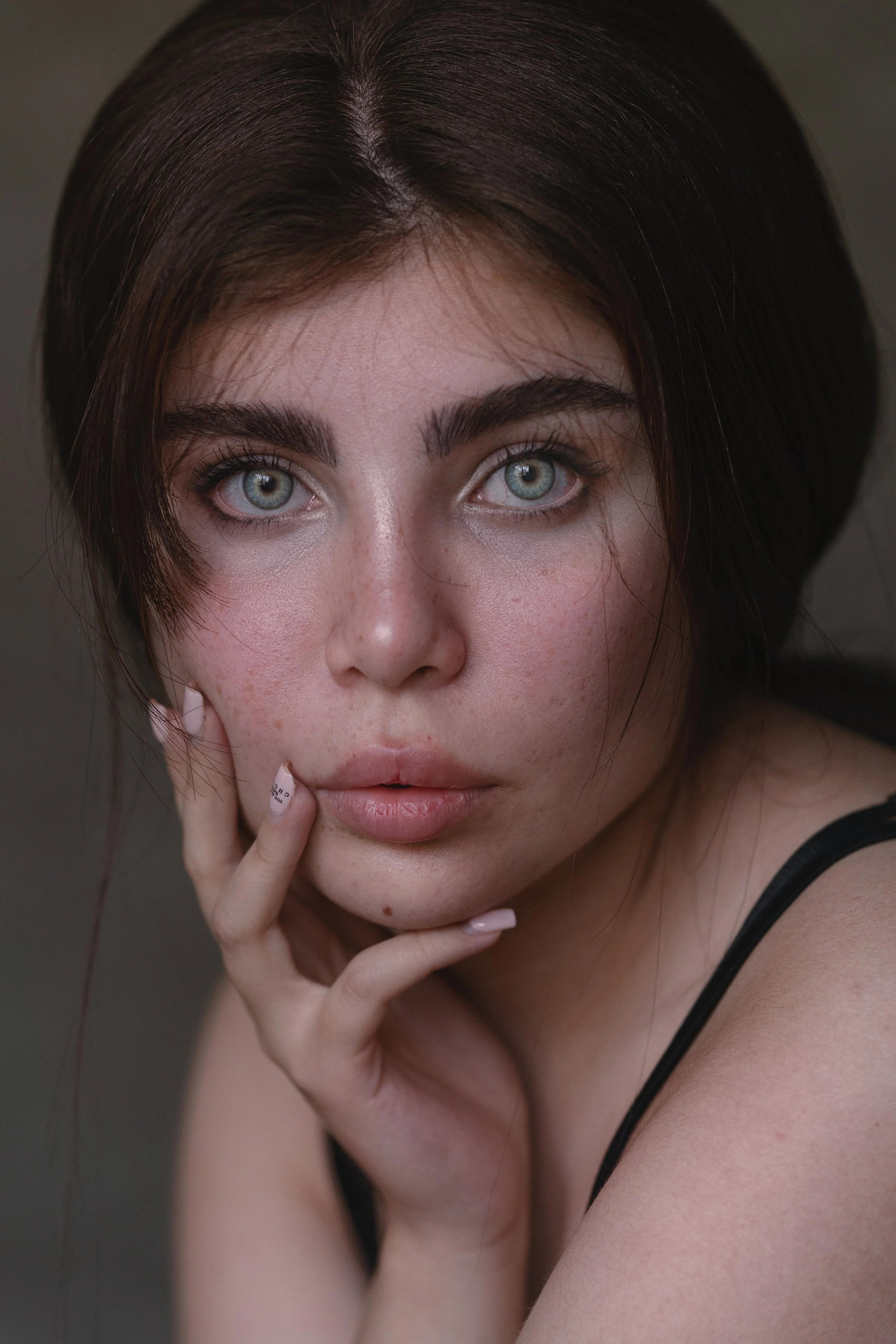 Close-up portrait of a woman with blue eyes and hand on face.