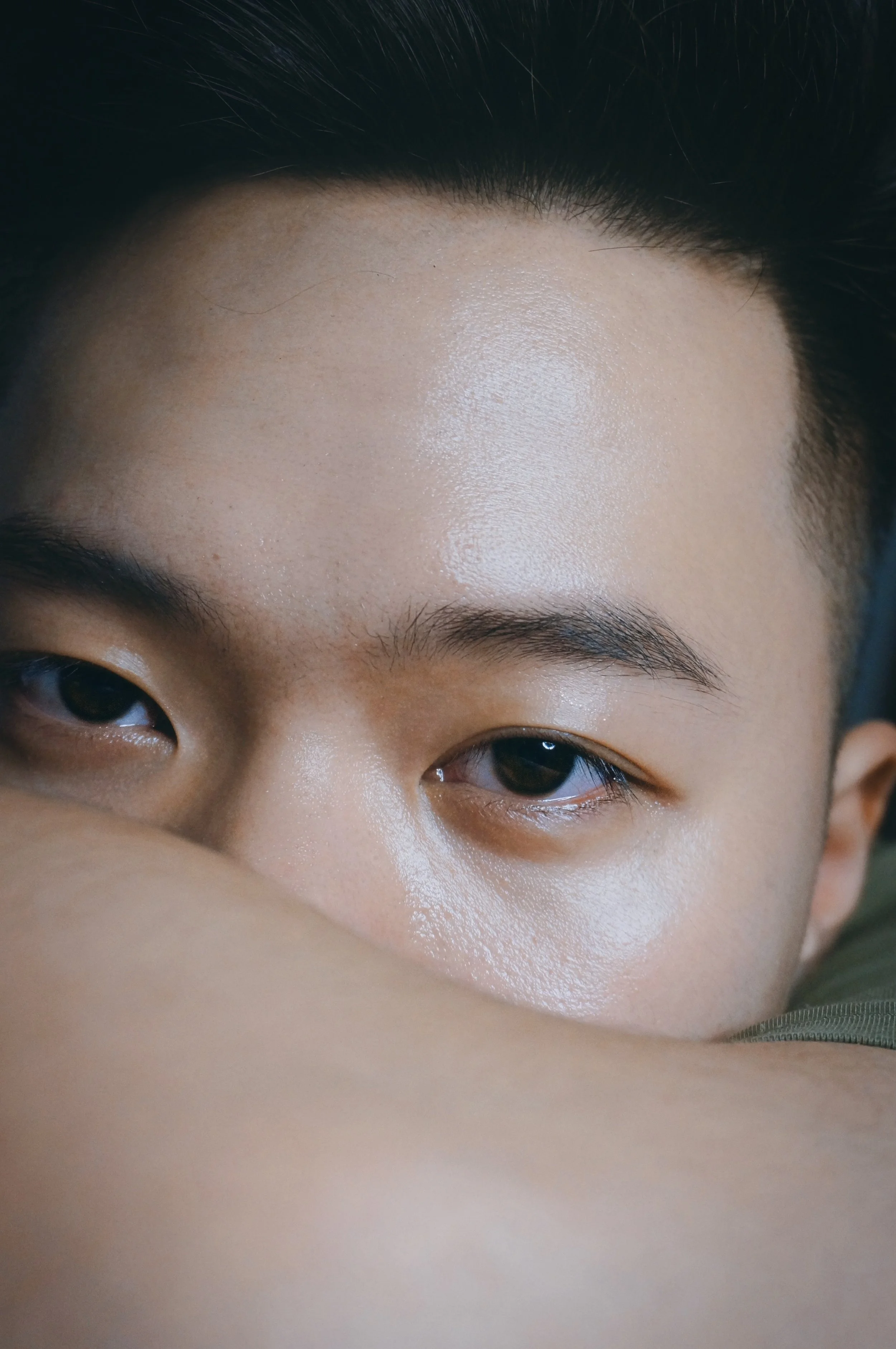 Close-up of a person's face partially covered by an arm, focusing on the eyes and forehead.