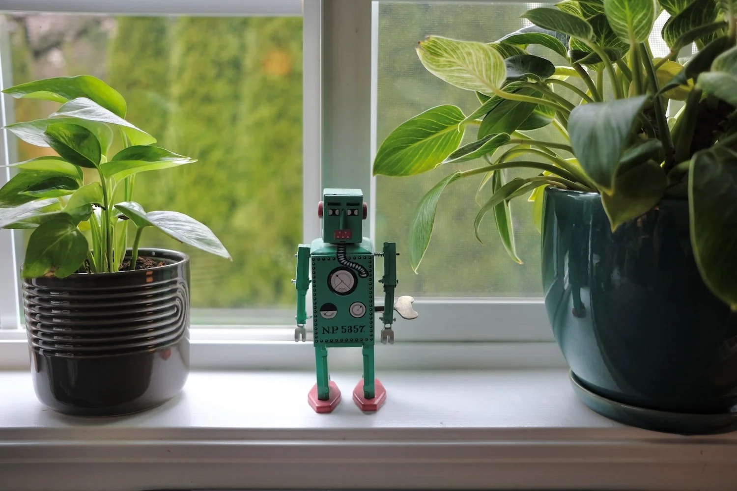 Image of green toy robot on a window sill with two plants for a post on AI and online course creation.