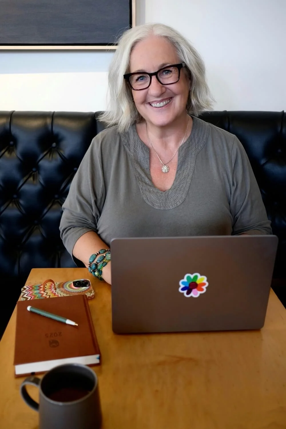 Calm Business Educator Kerstin Martin in a coffee shop with her laptop, Eule Planner, and a cup of coffee