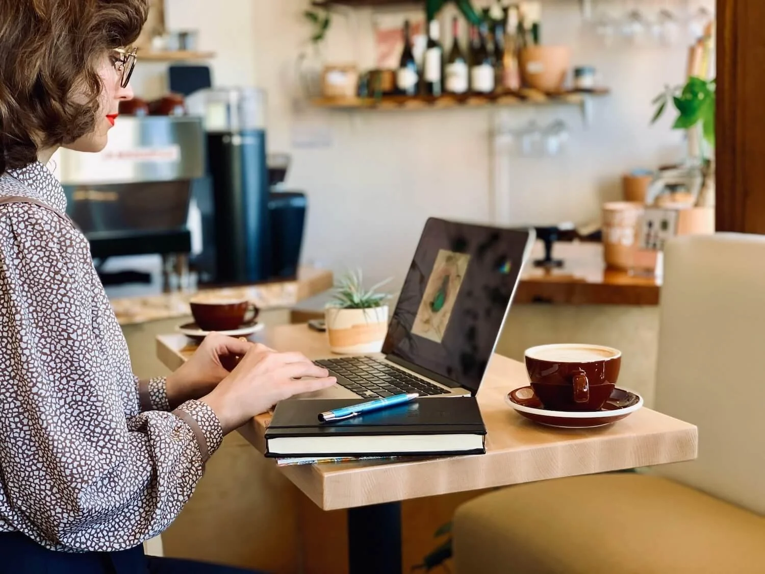 Photo of woman typing on a laptop with a Eule Planner and a cup of coffee next to her