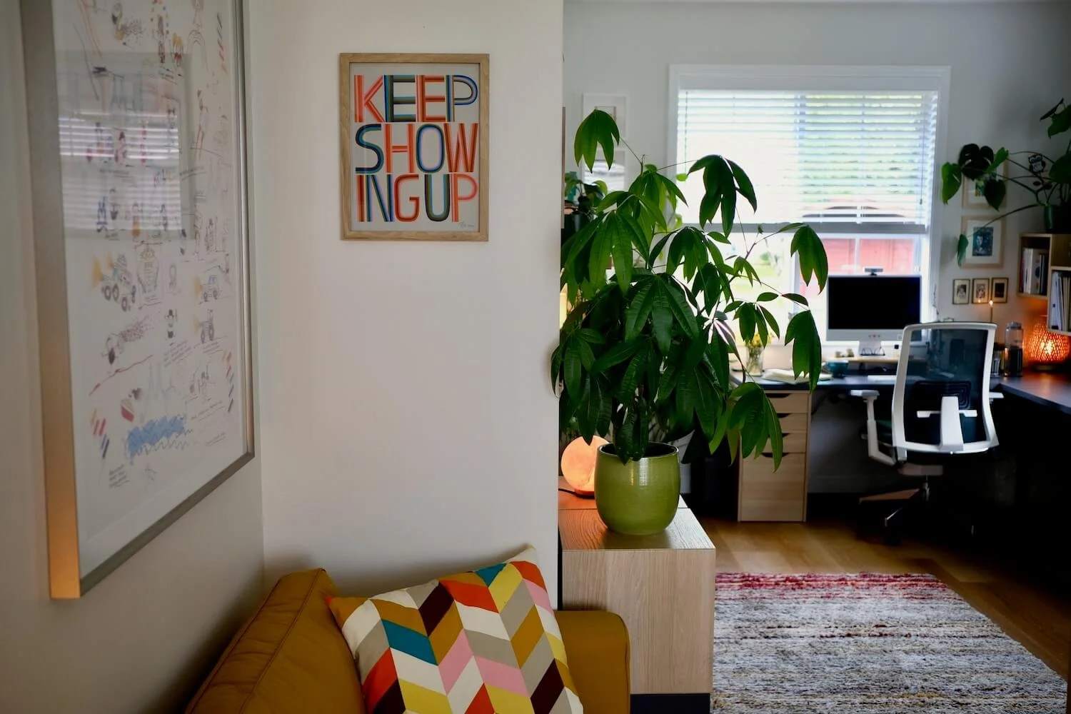 Photo of a home office with a desk and computer and a yellow sofa and a poster that reads KEEP SHOWING UP
