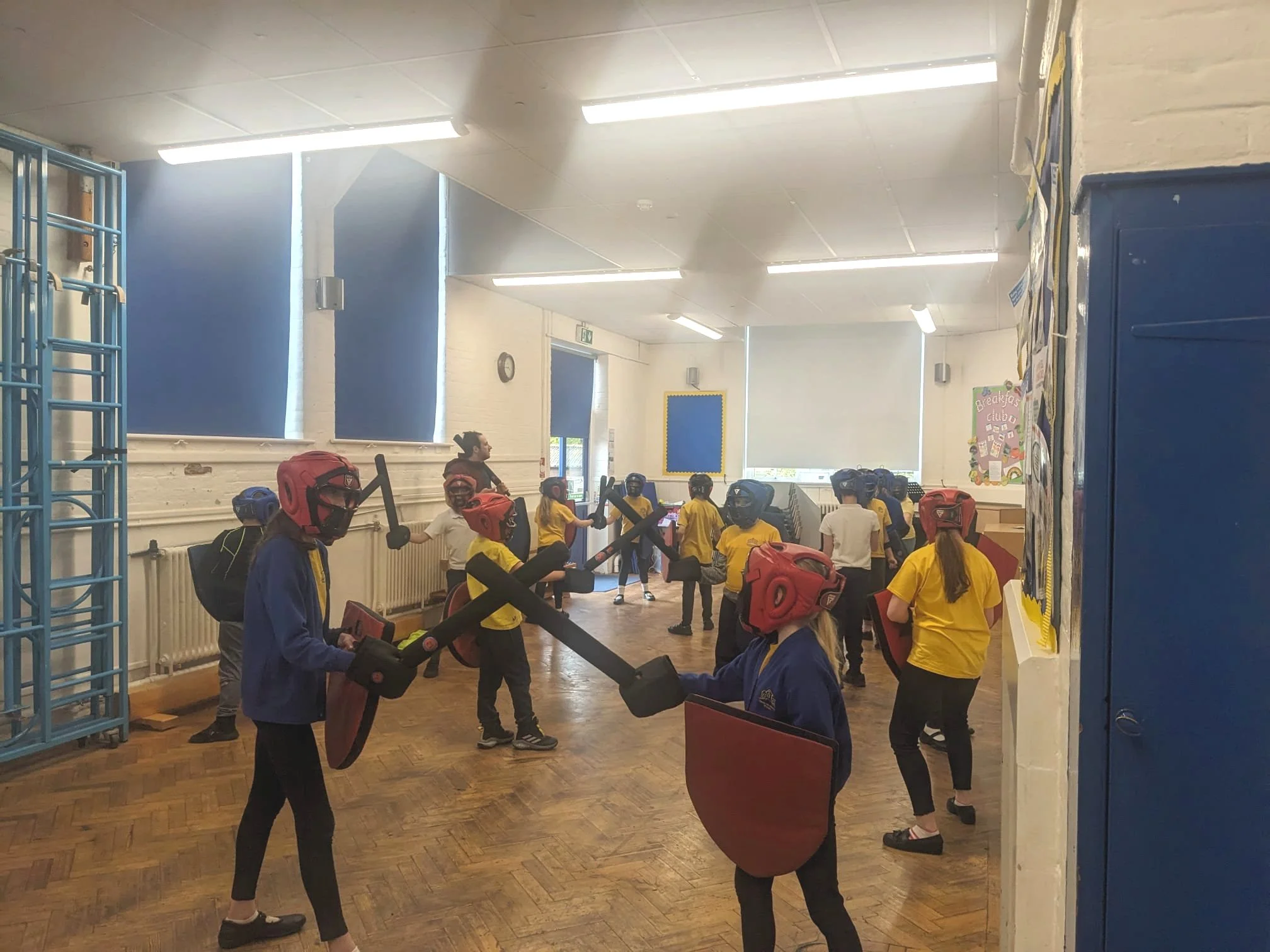 Class of students clad in soft kit preparing to sword fight in a school hall