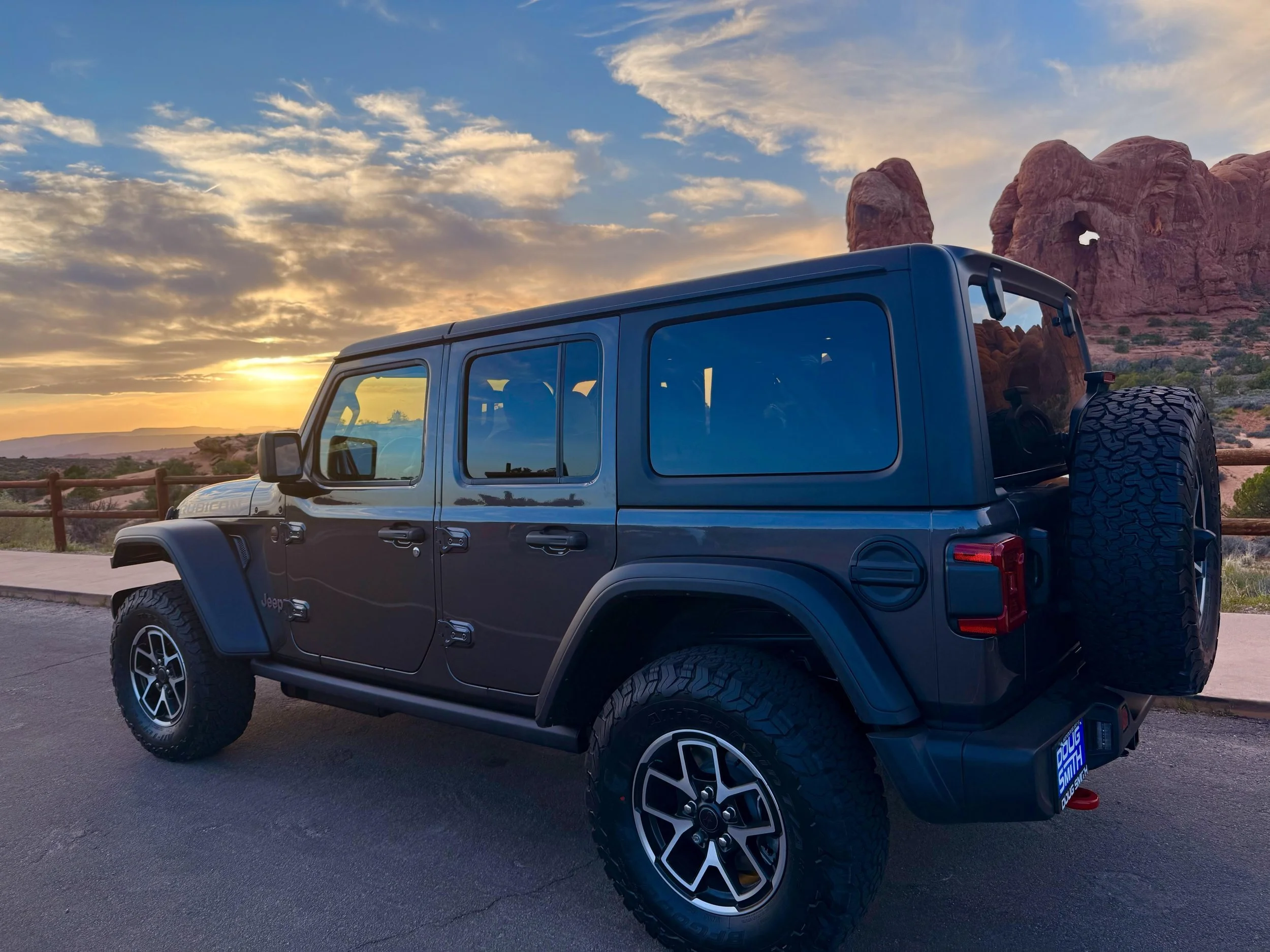 A black Jeep Wrangler parked at sunset with red rock formations in the background.