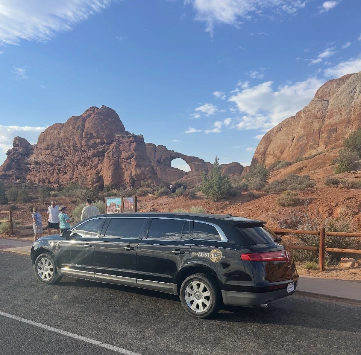 Moab Luxury Tours and Transportation stretch limo parked at the North/South Window Arches trailhead in Arches National Park, offering guests a front-row view of Turret Arch against Utah's iconic red rock formations.