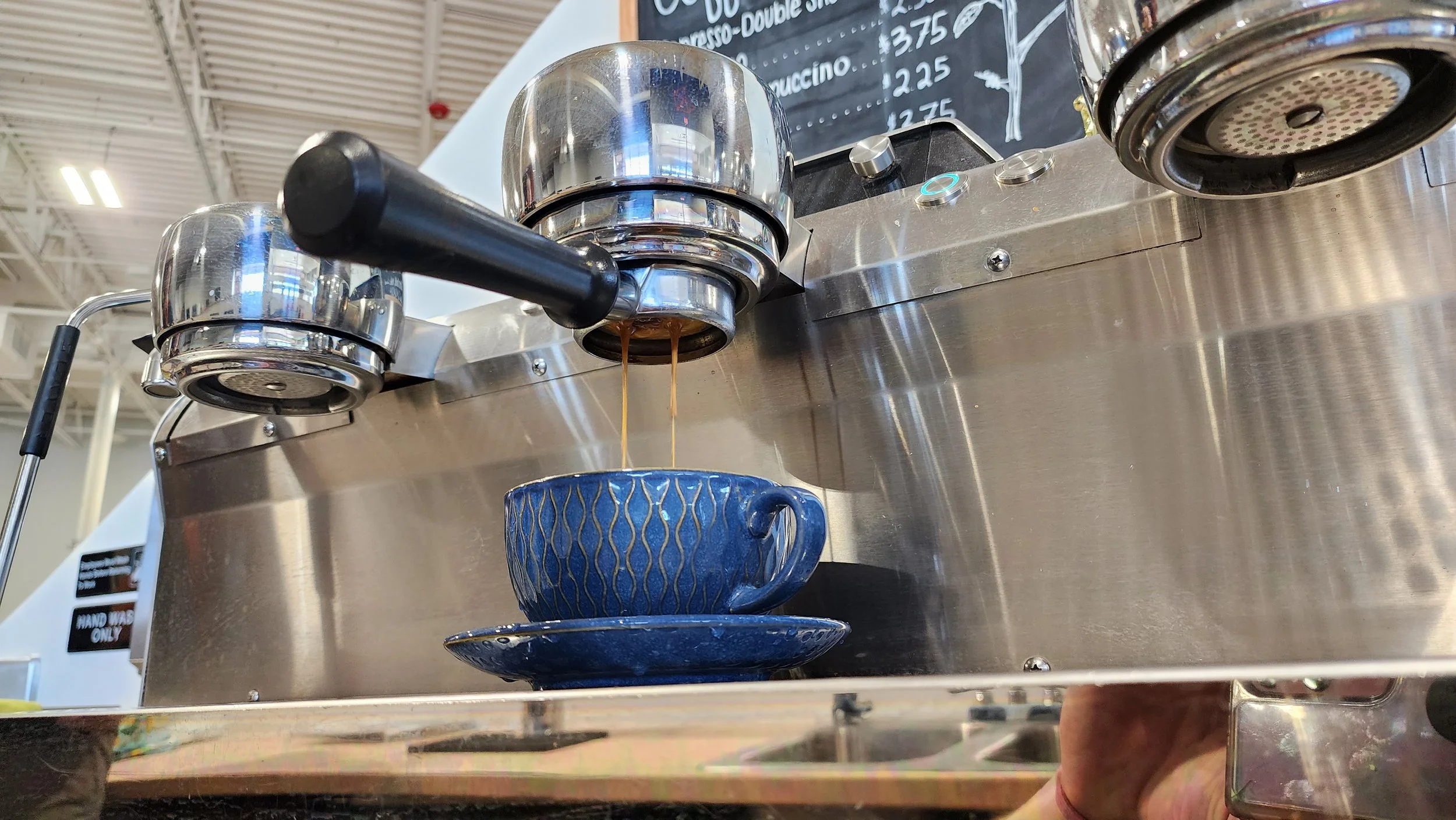 Close-up of a commercial espresso machine pouring espresso shots into a blue cup with a matching saucer underneath.