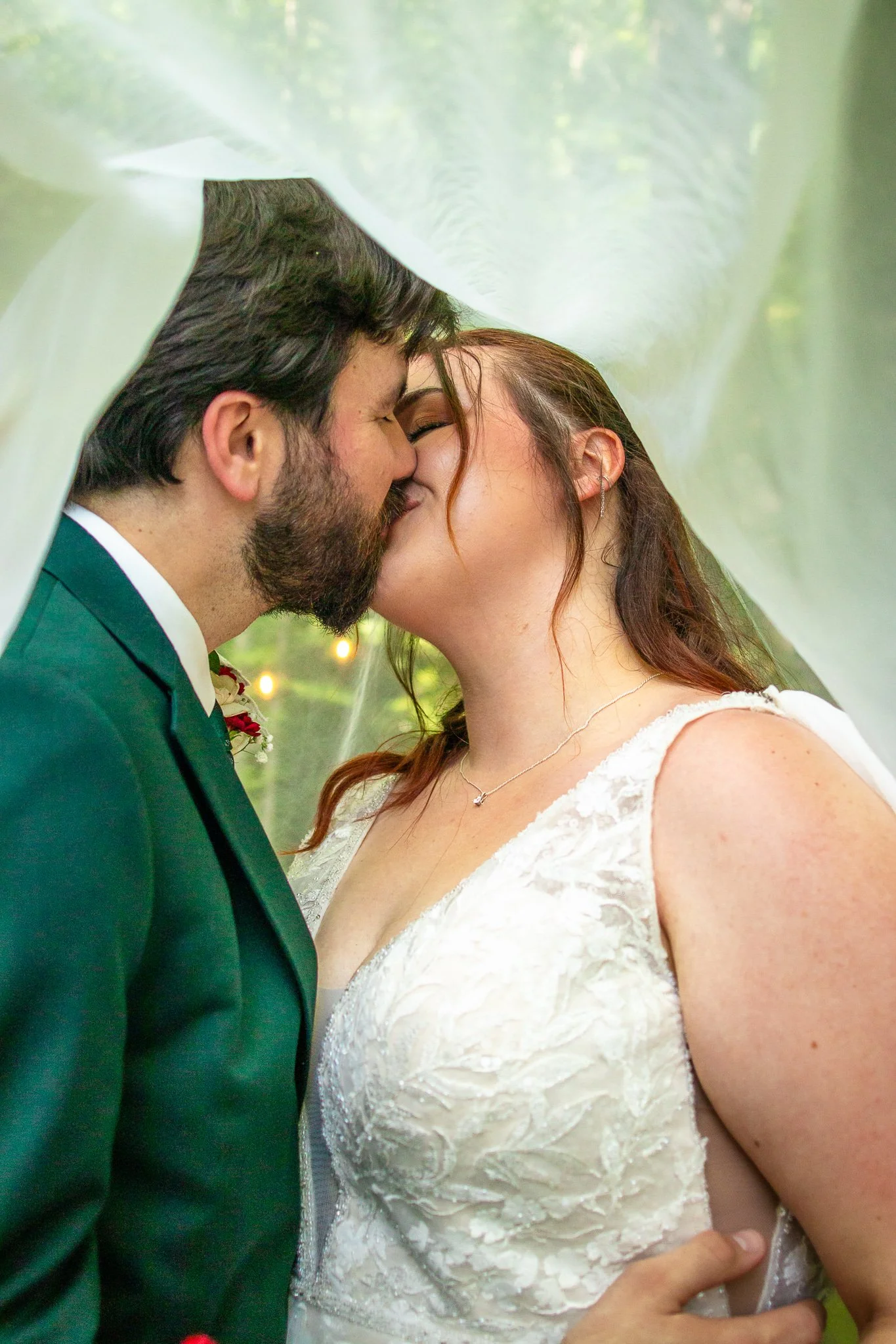 A close-up of a bride and groom sharing a kiss under a sheer white veil during their wedding.