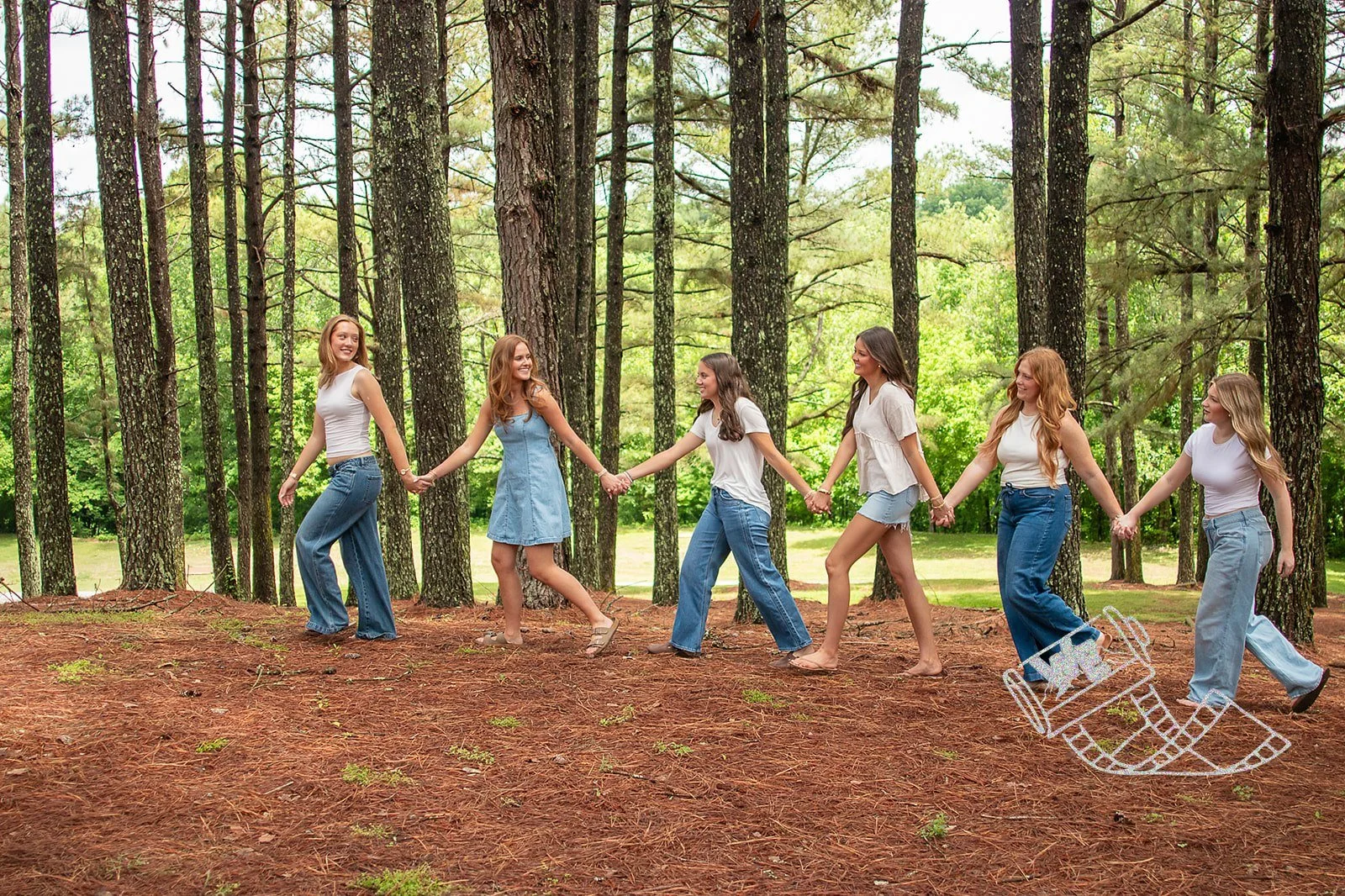 Seven young women holding hands in a circle outdoors in a forest, with leaves and trees surrounding them and a partly visible sketch of a rocking horse in the bottom right corner.