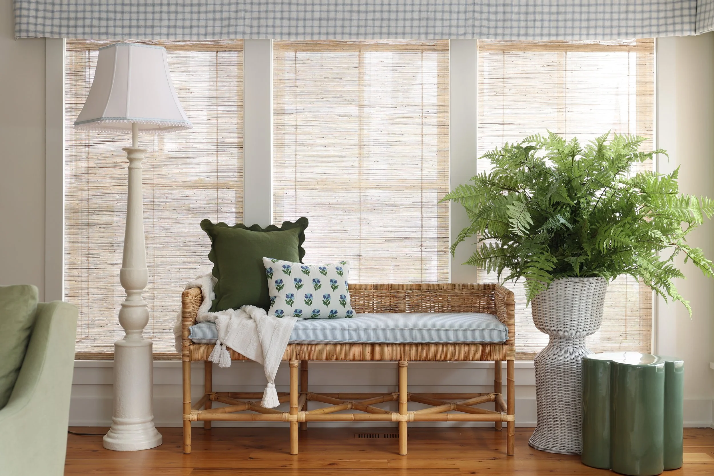 Sunlit living room with bamboo bench, large green potted fern, and a tall white floor lamp.