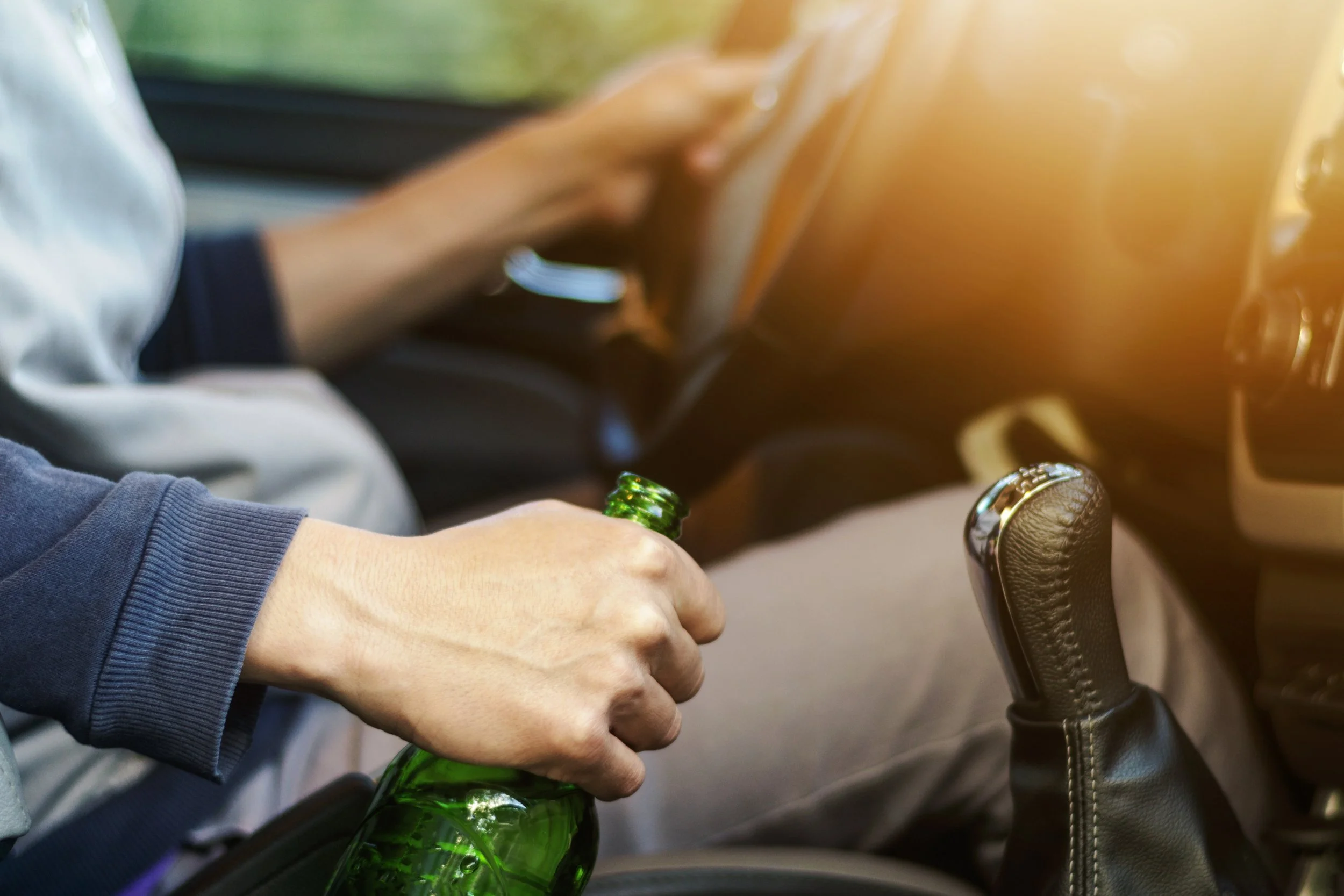 Man's hand holding a bottle of alcohol while driving