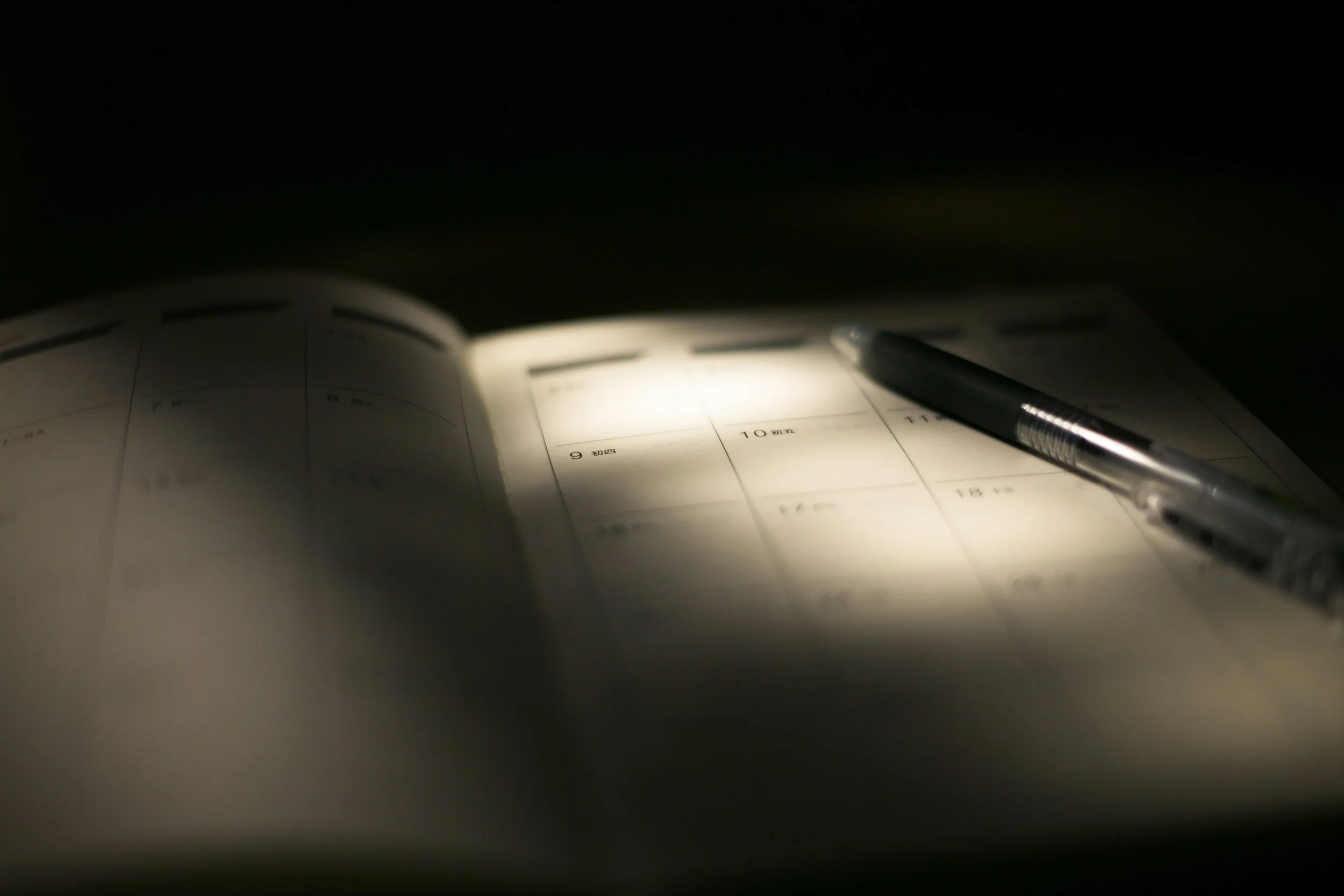 Open planner or calendar with a pen resting on it, illuminated in a dark setting.