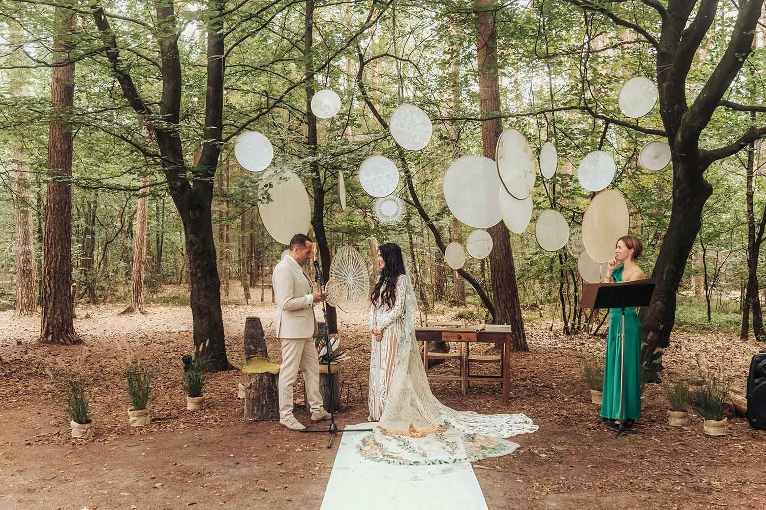An enchanting forest wedding ceremony unfolds, adorned with ethereal hanging decor, set amidst the tranquil trees – a perfect scene of an outdoor wedding in the forest.