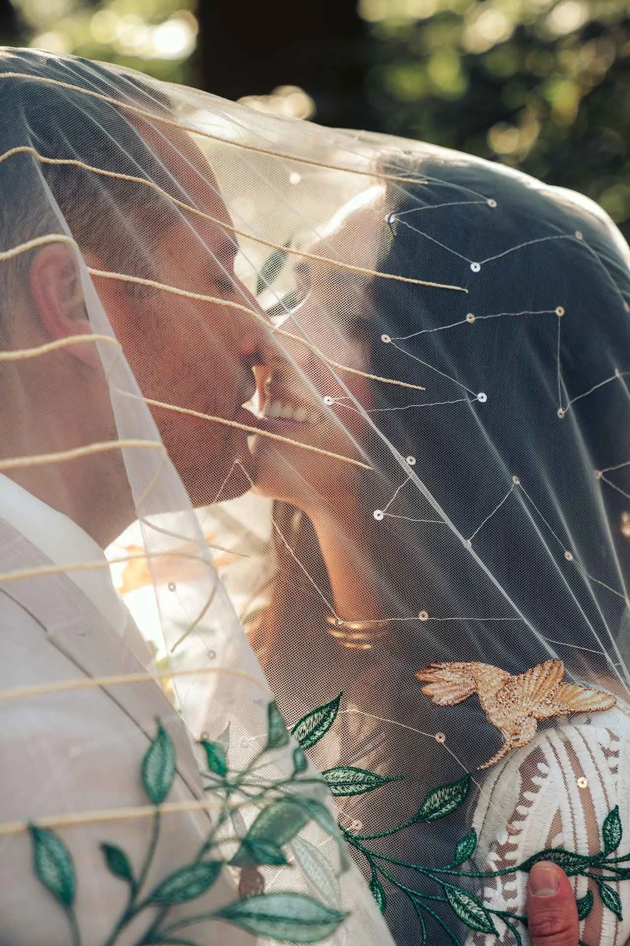 A close-up, intimate moment as a couple shares a kiss beneath a delicately embroidered veil, reflecting the profound connection of a Dutch wedding in the forest.