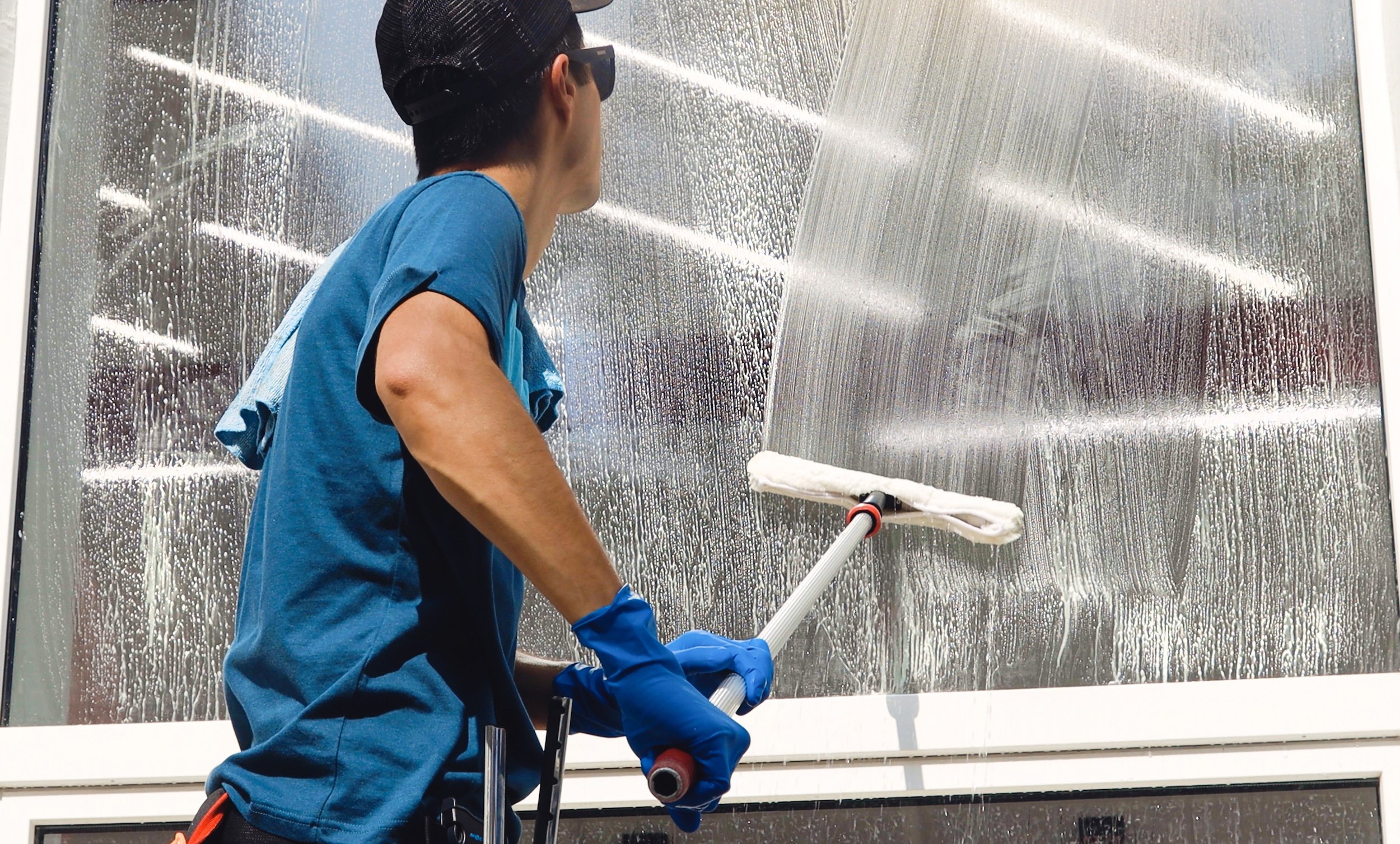 Male professional cleaning service worker in overalls cleans the windows and shop windows of a store with special equipment (Copy) (Copy)